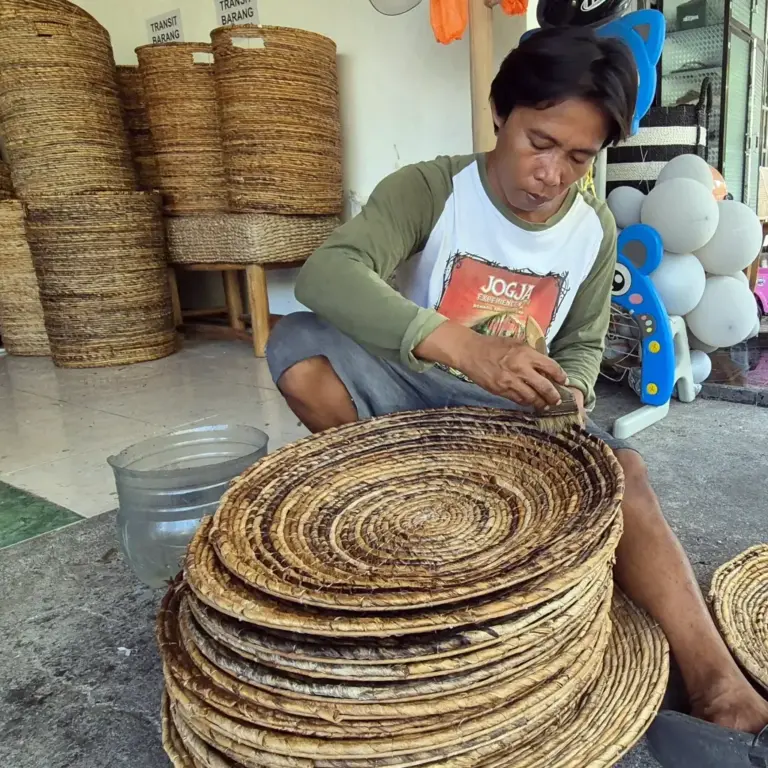 An Indonesian artisan meticulously hand-weaving natural fibers into intricate woven products, showcasing the traditional craftsmanship behind PT. Mitra Eco Bhavana's sustainable offerings